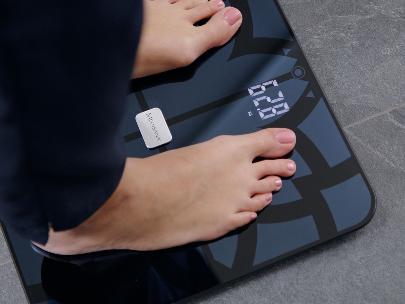 Füße einer Person stehen auf einer digitalen Glas-Körperwaage, die ein Gewicht von 62,8 kg anzeigt